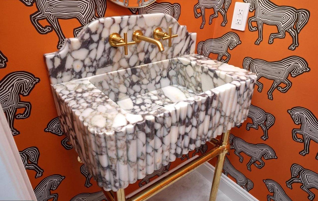 Powder room with a marble basin on a brass stand and bold patterned wallpaper